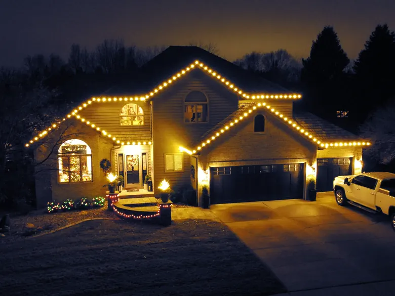 A two-story home outlined in warm white Christmas lights at dusk, installed by Sharp Lawn Care
