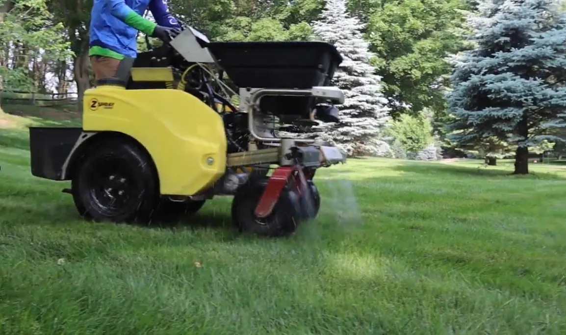 Sharp Lawn Care technician with spreader near truck servicing a Siouxland property