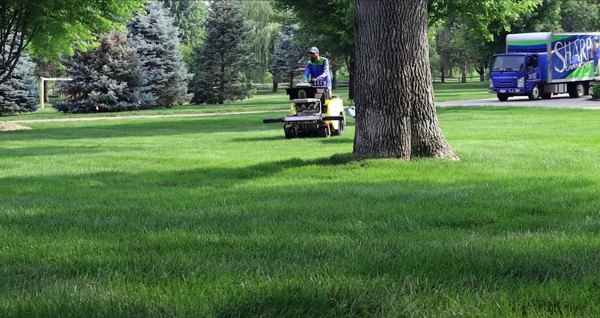Sharp Lawn Care technician fertilizing lawn with tow-behind spreader.