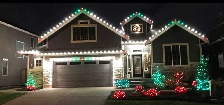 Warm white roofline Christmas lights with red bows and lit shrubs along the front beds