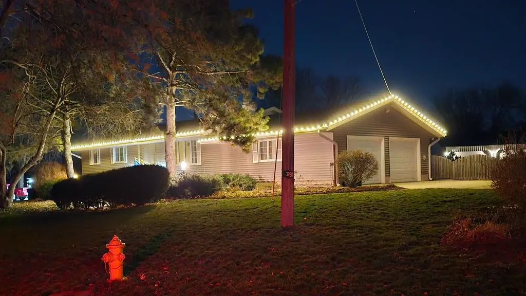 Christmas light installation on a Sioux City home, the full eave line lit at night with the front door framed to match