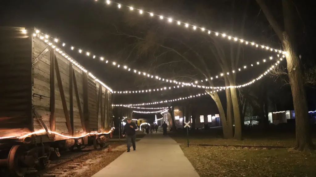 A canopy of string lights over the walking path at the Sioux City Railroad Museum, with a wooden boxcar lit alongside