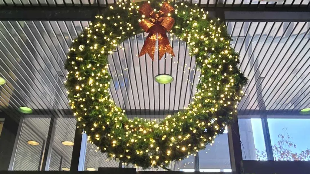 A large lit wreath with a red bow hanging high inside the glass entrance of a downtown Sioux City building