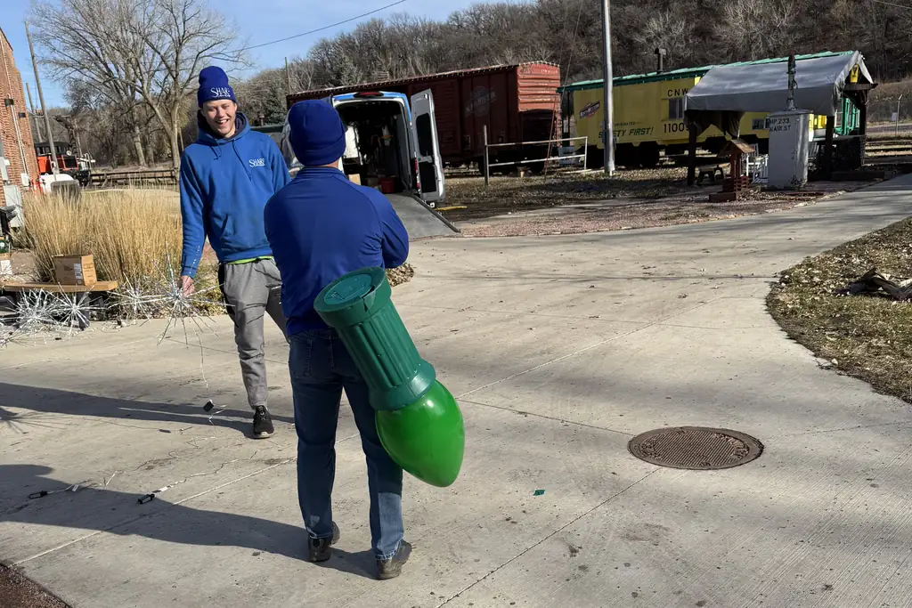 Two Sharp Lawn Care crew members carrying an oversized bulb prop across the staging yard
