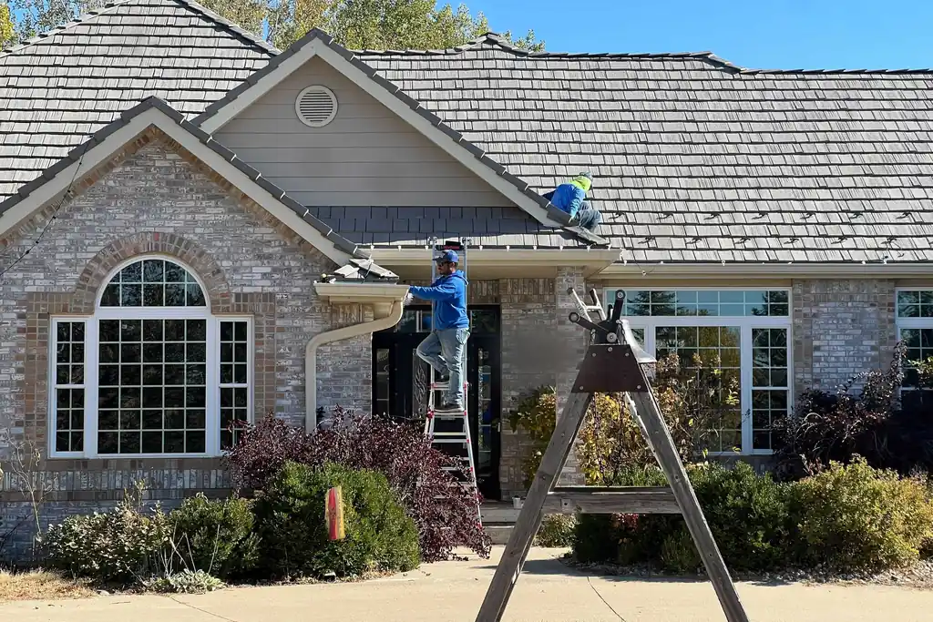 Two Sharp Lawn Care technicians working a Sioux City roof in daylight with the ladder set