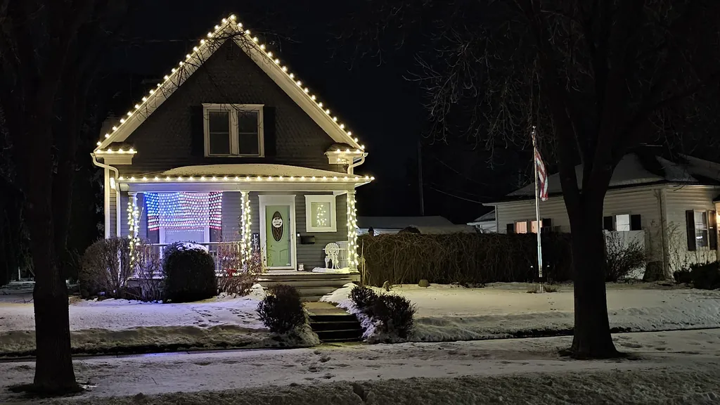 An older gabled two story home on a snowy Sioux City street lit for Christmas