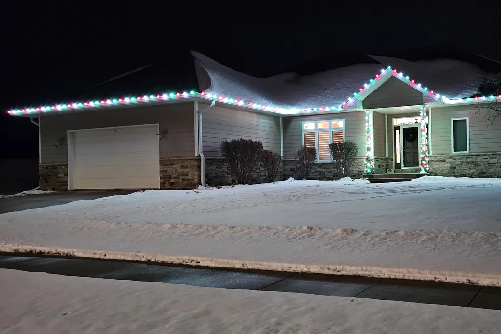 A Sioux City home lit at night with the roof line and the porch columns picked out