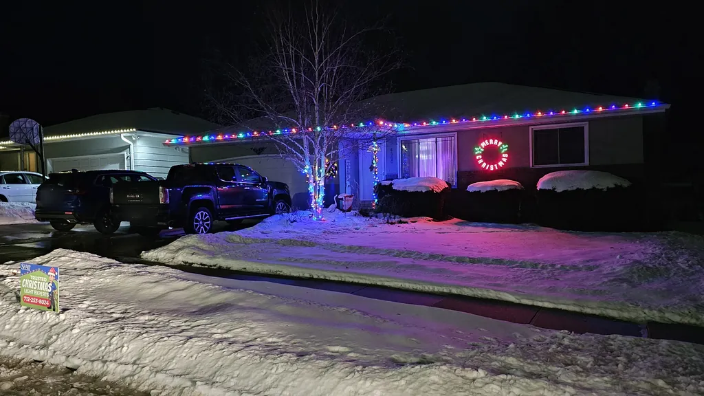 A wide view across a snowy Sioux City street with a Sharp Lawn Care yard sign at the edge