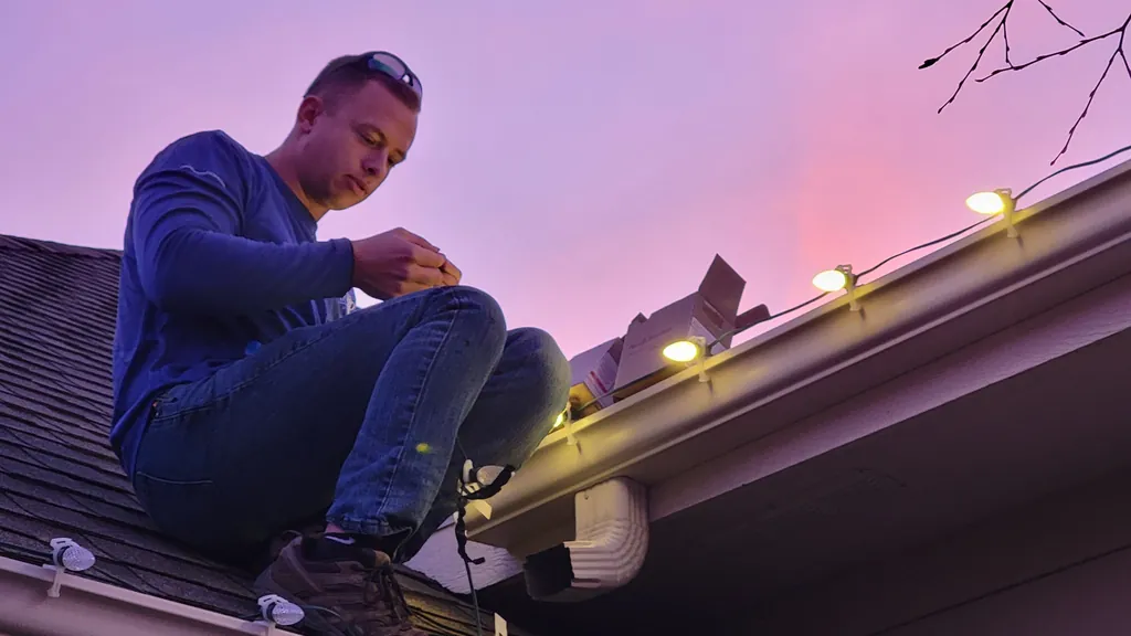 A Sharp Lawn Care technician clipping a bulb to a shingle roof at sunset in Sioux City