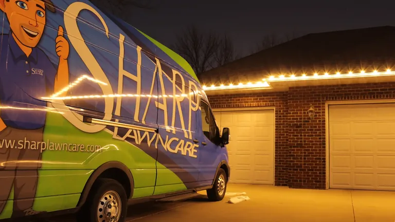 Warm white roofline and garage Christmas lights on a ranch at night with a Sharp van in the driveway