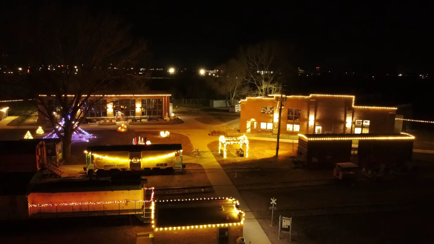 An elevated rail yard display at a Siouxland landmark after dark, with the buildings outlined in lights and the rolling stock lit