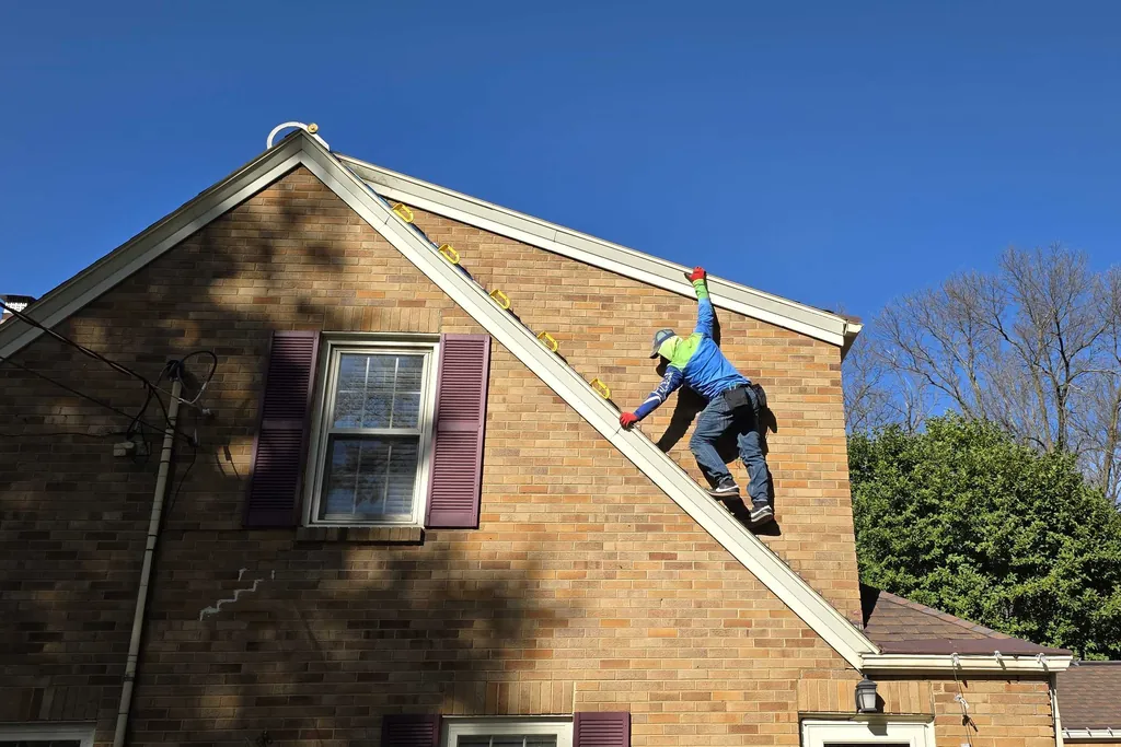 A Sharp Lawn Care technician climbing a steep gable to run a roof line of Christmas lights