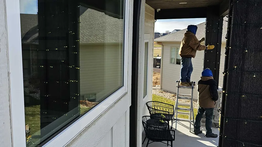 A view along a covered porch to a Sharp Lawn Care technician on a ladder with bulbs in hand