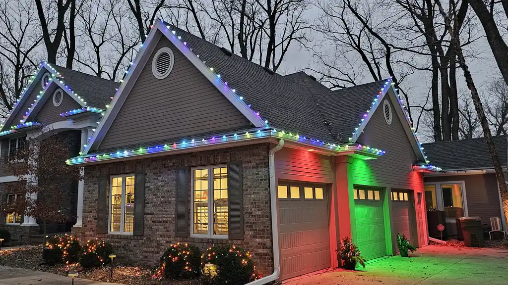 A two story Sioux Falls home in mature oaks with mixed color Christmas lights along every gable