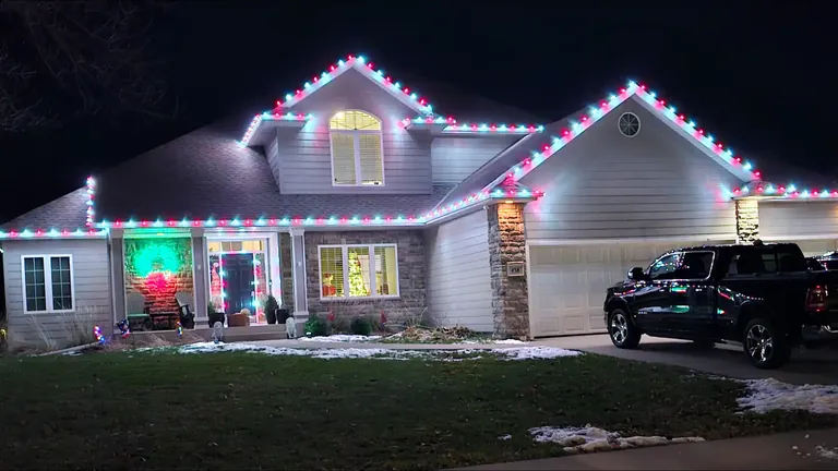 Warm white holiday lights along the full roofline of a Sioux Falls home at night with the entry framed to match