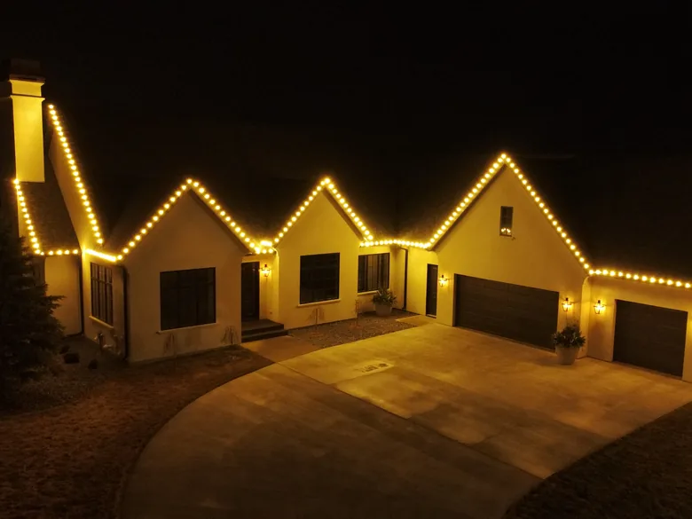 A stucco ranch home in Sioux Falls at night with warm white Christmas lights along every roofline and a lit entry